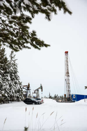 Pump jack and oil rig in the oilfield situated in the beautiful winter forest. Environmental pollution. Oil and gas concept.の写真素材