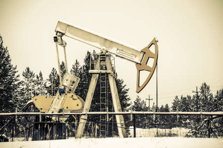 Horizontal view of a pump jack in the oilfield situated in the beautiful winter forest. Environmental pollution. Oil and gas concept.の写真素材