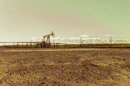 Oil pumps in the oil field. Summer hot sunny day. Seagulls soaring in the sky. Minimalistic industrial landscape.の写真素材