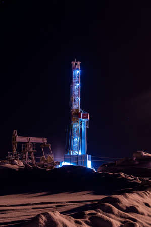 Oil and Gas Drilling Rig at night. Drilling rig and pump jack operation on the oil platform.