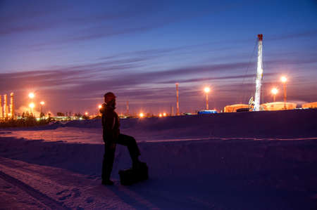 Oil worker in oilfield. Pump jack and engineer on a winter sunset sky background. Western Siberia.の写真素材