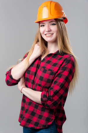 Portrait of a young attractive woman with blond hair in orange helmet on a neutral gray background.の写真素材