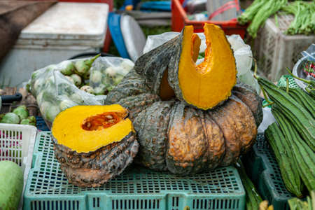 Selling on the open market in the street a green ornamental cut pumpkin with seeds surrounded by other vegetables. Vegetarian and healthy lifestyle. Gourds and squashes. Organic food.の写真素材