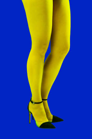 Close-up picture of womans beautiful yellow legs in high heels shoes on acid blue color background....