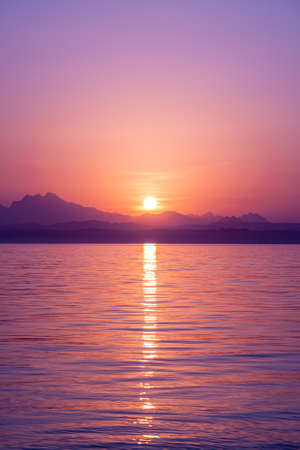 Stunning seascape on beautiful colorful sunset. The sun hides in the mountains and reflected in calm...