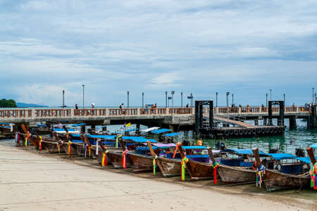 Parking of tieded traditional thai longtail boats with colorful tape, Thailand. Waiting for passenger. Tourists on the pier on blue sky background. Ships, yachts and fishing boats at low tide.の写真素材