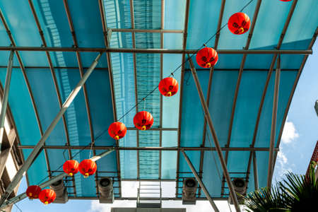 Asian traditional bright red lanterns hanging at street with blue glass roof on background for...