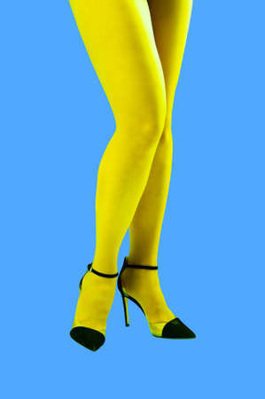 Close-up picture of womans beautiful yellow legs in high heels shoes on acid blue color background. Disco lights. Fasion. Surreal art. Funny modern art collage. Pop art. Zine culture. Front view.の写真素材