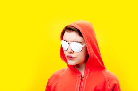 Close up fashion portrait young beautiful woman in hoodie and white glasses. Alternative funky girl on a bright yellow background. Unusual youth fashion concept. Hot image.の写真素材