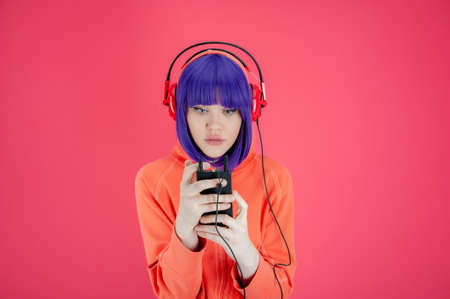 Portrait funky beautiful young woman with blue hair in hoodie on bright pink background. Alternative girl with headphone listens cool music in her smartphone. Unusual youth fashion concept. Hot image.の写真素材
