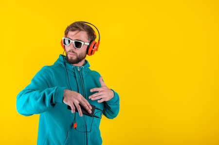 Funky young bearded hipster man in glasses and headphones dances and listens pleasurable music in...