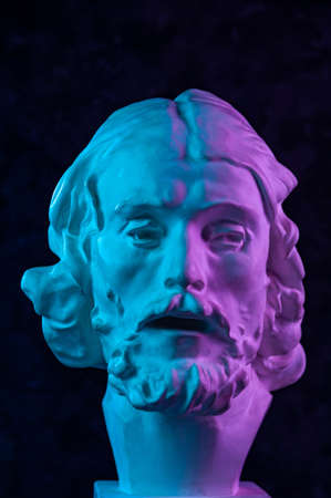 Colorful gypsum copy of ancient statue of John the Baptist head for artists on a dark textured background. Plaster sculpture man face. John baptized Jesus. Art poster in purple and blue bright colors.の写真素材