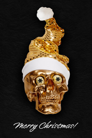 Gold spooky skull in bright golden Santa Claus hat on textured black background. Funky xmas decor. Crazy concept of holidays, cool party, 2023 New Year and Merry Christmas. Winter funny holiday moodの写真素材