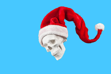 White spooky skull in bright red Santa Claus hat isolated on blue background. Funky hard xmas decor. Crazy concept of holidays, cool party, 2023 New Year and Merry Christmas. Winter funny holiday moodの写真素材