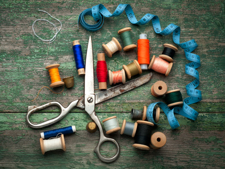 Vintage with sewing tools and colored tape/Sewing kit. Scissors, bobbins with thread and needles on the old wooden の写真素材
