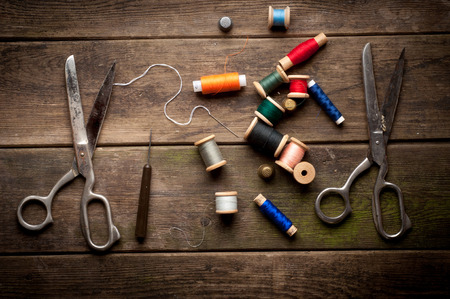 Vintage Background with sewing tools and colored tape. Sewing kit. Scissors, bobbins with thread and needles on the old wooden backgroundの写真素材