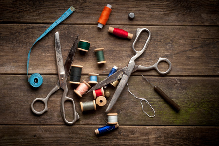 Vintage Background with sewing tools and colored tape. Sewing kit. Scissors, bobbins with thread and needles on the old wooden backgroundの写真素材