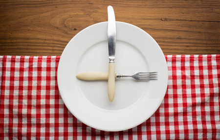 Empty plate with fork and knife on tablecloth over wooden backgroundの写真素材