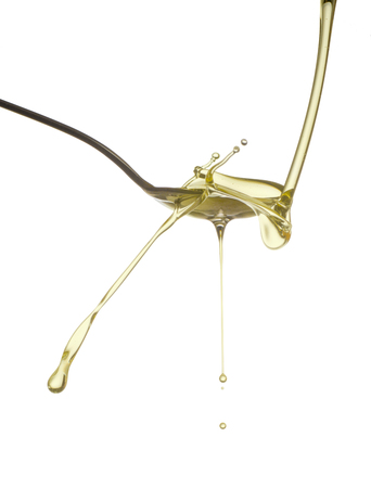 Pouring oil splash on spoon. Isolated on white background.の写真素材