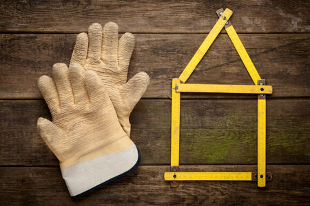 House concept with yellow meter and working gloves on wooden background