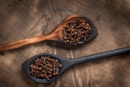 Cloves in wooden spoon on old wooden background, flat layの写真素材