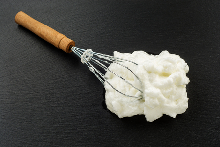 Process of cooking meringue. Whipped egg whites on whisk on slate background. Baking dessert conceptの写真素材