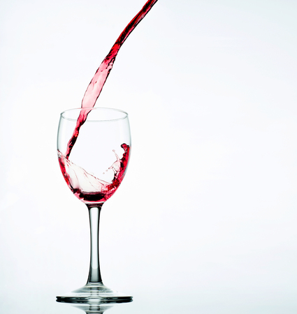 Pouring red wine in glass goblet isolated on whiteの写真素材