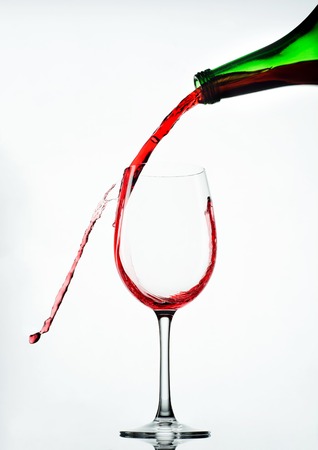 Pouring red wine in glass goblet isolated on whiteの写真素材