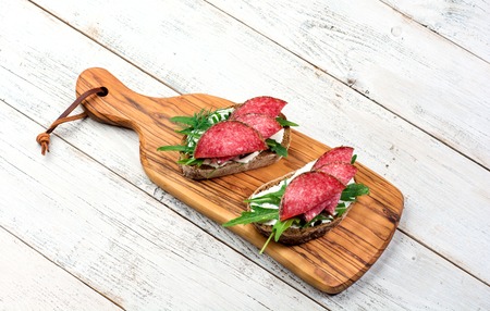 Two fresh sandwiches with salami , cheese, bacon, tomatoes, lettuce and arugula light wooden backgroundの写真素材