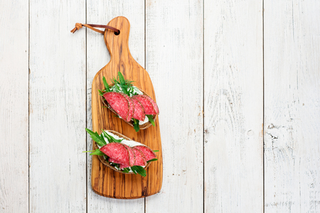 Tasty appetizer of thinly sliced spicy salami on bread with cheese and herbs on a cutting board with copy spaceの写真素材