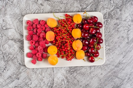 mixed many different colorful seasonal fruits, raspberries, cherries, apricots, on plate, top view, copy spaceの写真素材