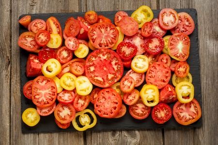 Variety of ripe fresh organic gardening tomatoes different kind and colors with water spot and basil leaves in wood tray over old grey wooden background. Flat lay, copy spaceの写真素材
