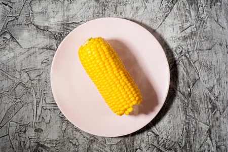 Ripe boiled corn on a pink plate on concrete table, top viewの写真素材