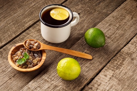Glass of hot tea with lime, lemon, mint and brown sugar on old wooden table. Dark rustic style.の写真素材