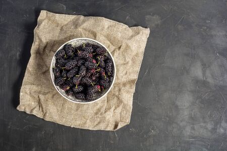 Fresh raw black mulberries in plate on dark concrete background. Top view with copy space. Flat lay background.の写真素材