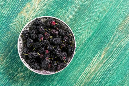 Fresh raw black mulberries in plate on green wooden background. Top view with copy space. Flat lay backgroundの写真素材