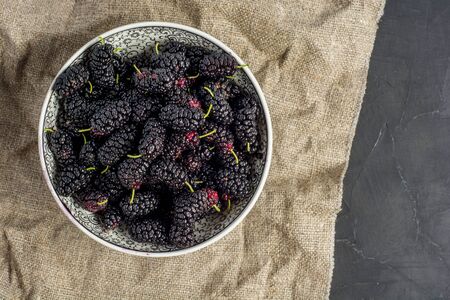 Fresh raw black mulberries in plate on dark concrete background. Top view with copy space. Flat lay backgroundの写真素材