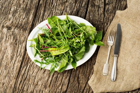 Healthy fresh green salad leaves on plate with cutlery on rustic wooden background.の写真素材