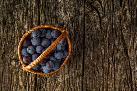 Flat lay. Fresh organic plums in basket on rustic wooden tableの写真素材