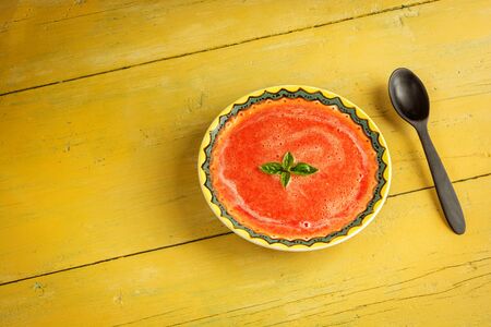 Gazpacho soup with green basil in yellow bowl on rustic background. Traditional spanish cold soup puree.の写真素材