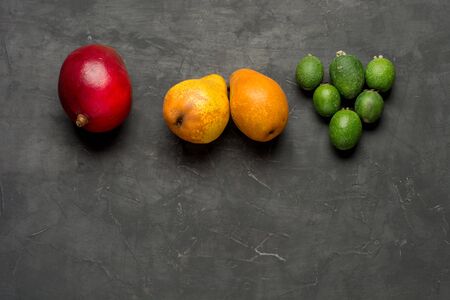 Healthy vegetarian food on dark concrete background. Delicious fruits on dark background. Mango, pear, feijoa . top view or flat lay with copy space.の写真素材