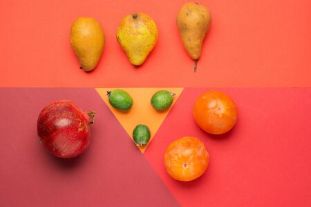 Healthy vegetarian food on colorful background. Delicious fruits on red background. Pomegranate, pear, feijoa and persimmon. top view or flat lay with copy space.の写真素材