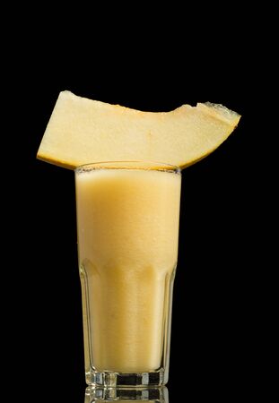 Glass of delicious melon smoothie with slice of sweet melon isolated on black gackgroundの写真素材