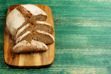 Yeast free, no knead, unleavened healthy organic rye wheat half sliced homemade bread loaf on kitchen board on green wooden table.の写真素材