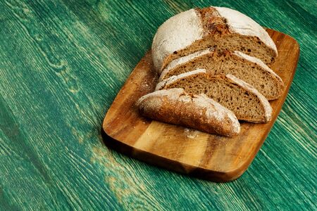 Yeast free, no knead, unleavened healthy organic rye wheat half sliced homemade bread loaf on kitchen board on green wooden tableの写真素材