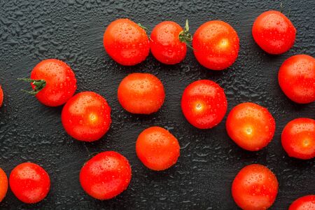 Fresh cherry tomatoes on a black background with water drops. Top view or flat lay. Minimal black stile.の写真素材