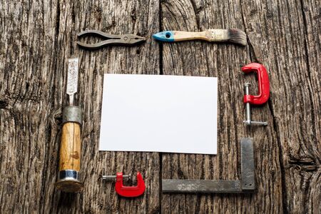 Old carpenter tools on rustic wood table with blank paper top view.