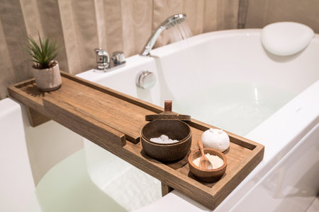 Modern and comfortable bathroom, Bath tub with wooden table and toiletries, Salt, Herb, Bath Bomb.の写真素材