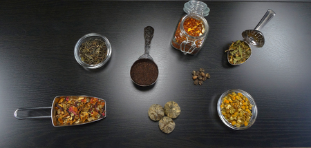 Tea composition with tea and flowers, jasmine, chamomile, black tea, health tea at black wooden backgroundの写真素材