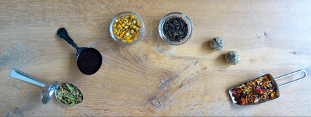 Tea assortment at spoons ant loose tea flowers at wooden background